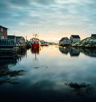 A fishing harbour at first light, weathered sheds reflected in still water.